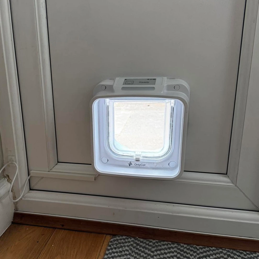 A customer’s OnlyCat installed in a white door, with the cable routed beside the frame